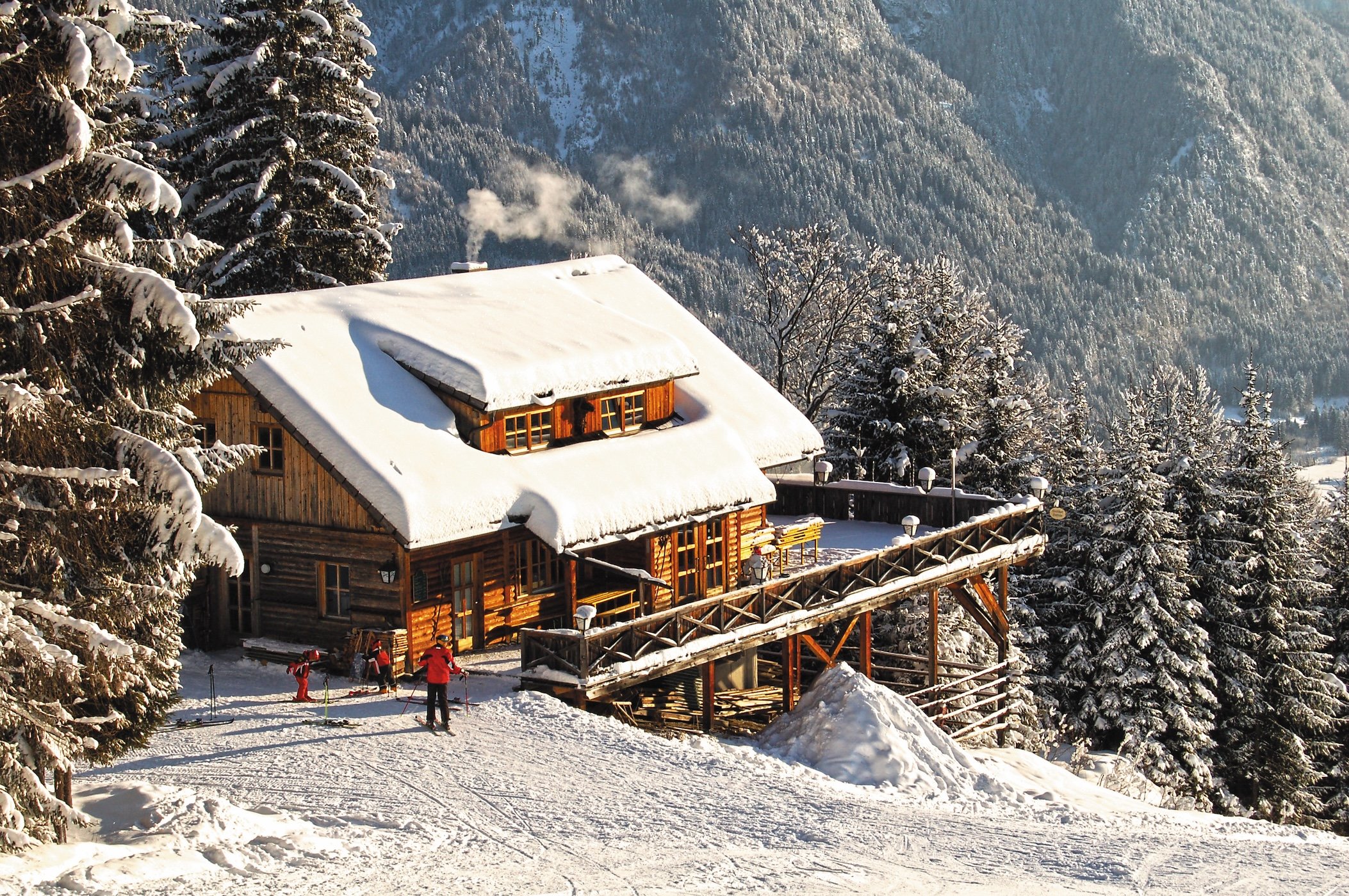 Verschneite Hütte mit Skifahrern am Waldrand