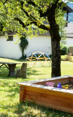 Sandkasten unter Baum mit Spielzeug und Wiese