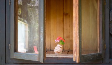 Hand mit Blumenstrauß durch offenes Holzfenster