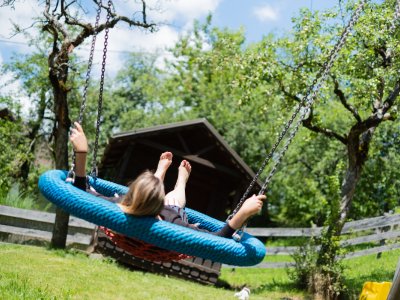 Frau schaukelt in blauer Nestschaukel im Garten