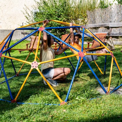 Kinder spielen in bunter Kletterkuppel auf Wiese