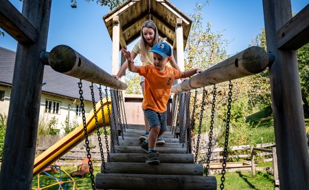 Zwei Kinder überqueren gemeinsam die Hängebrücke aus Holz