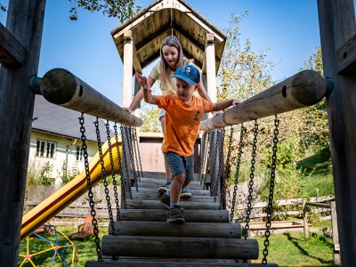 Zwei Kinder überqueren gemeinsam die Hängebrücke aus Holz