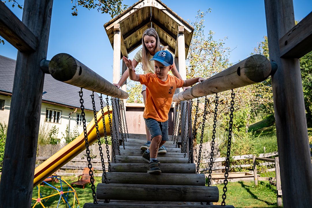 Zwei Kinder überqueren gemeinsam die Hängebrücke aus Holz