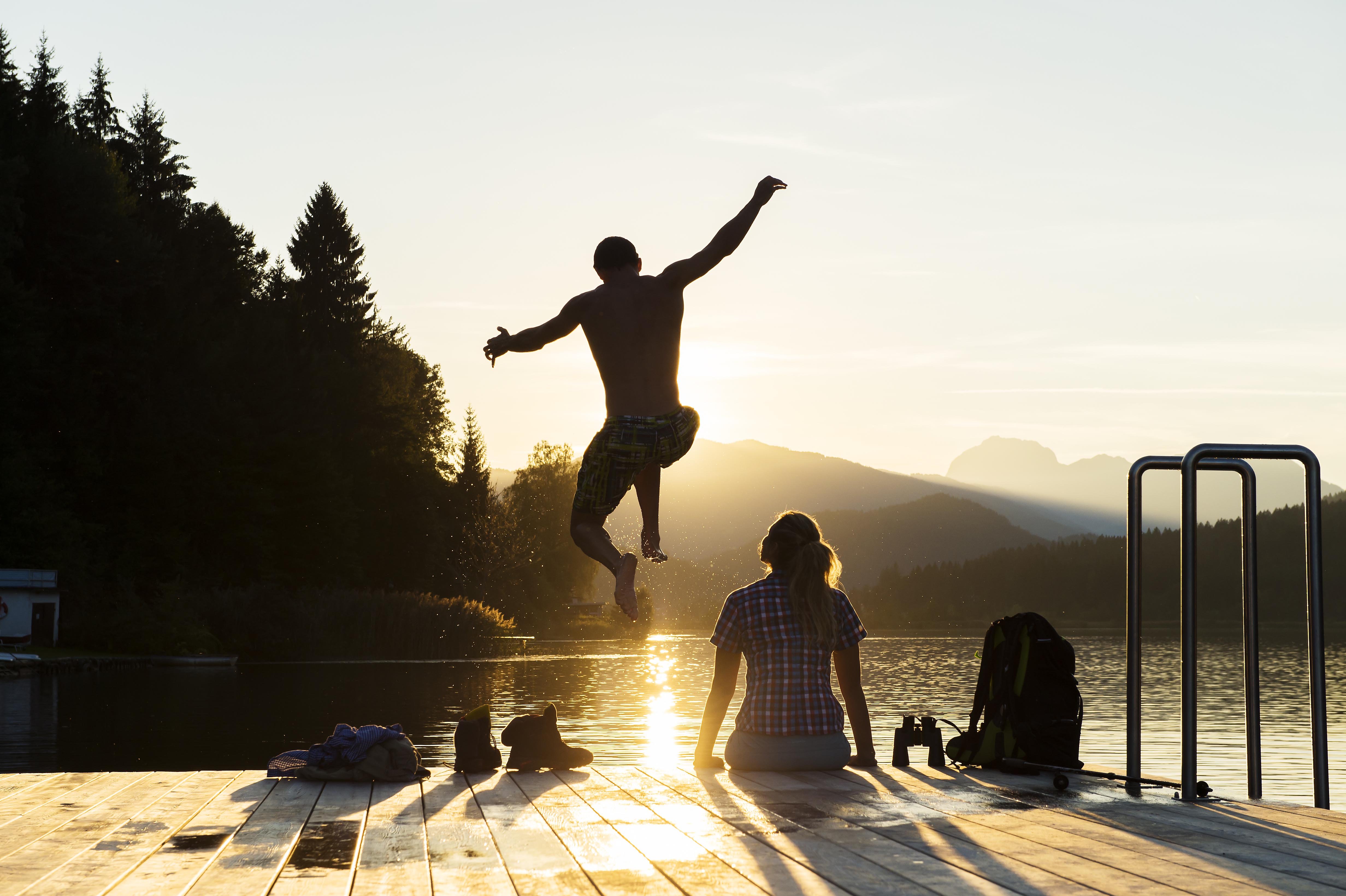 Mann springt vom Steg ins Wasser bei Sonnenuntergang