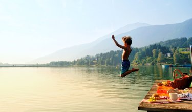 Boy jumping from the dock into lake next to a picnic