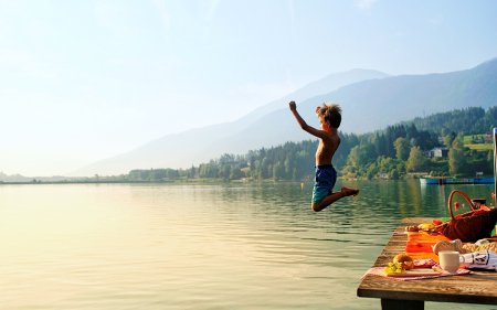 Boy jumping from the dock into lake next to a picnic