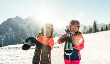 Zwei Kinder halten stolz ihre Skier in der Hand