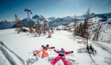 Zwei Kinder machen Schneeengel im Pulverschnee