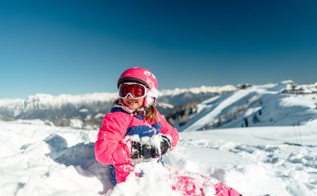 Mädchen sitzt lachend im Schnee mit Skibrille