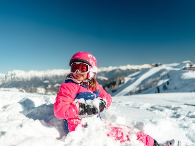 Mädchen sitzt lachend im Schnee mit Skibrille
