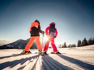 Kinder mit Skiern im Sonnenlicht am Hang