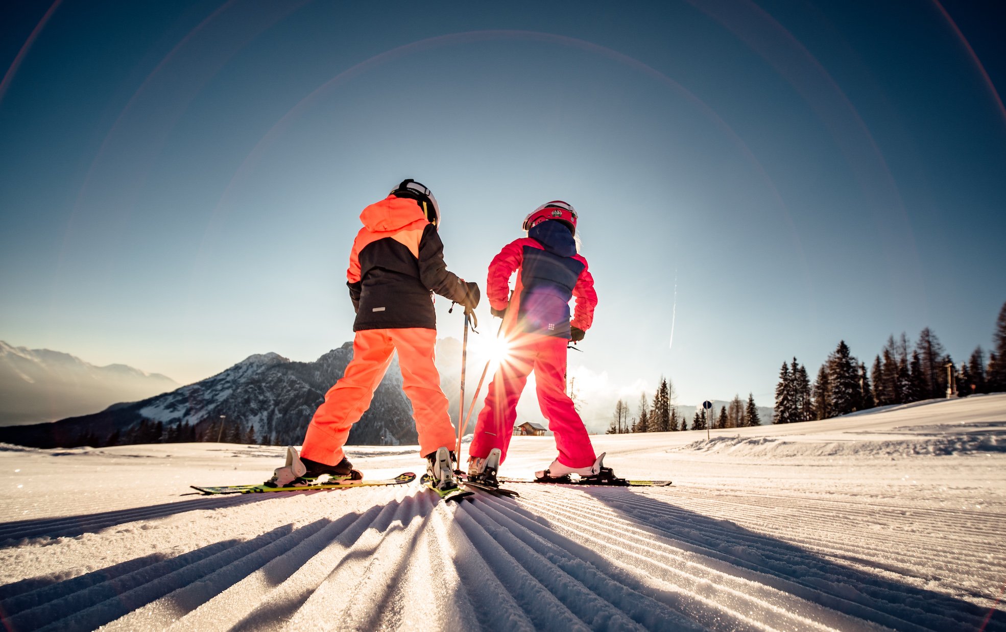 Kinder mit Skiern im Sonnenlicht am Hang
