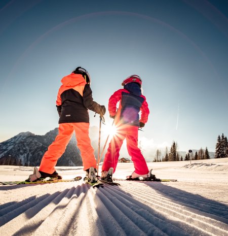 Kinder mit Skiern im Sonnenlicht am Hang
