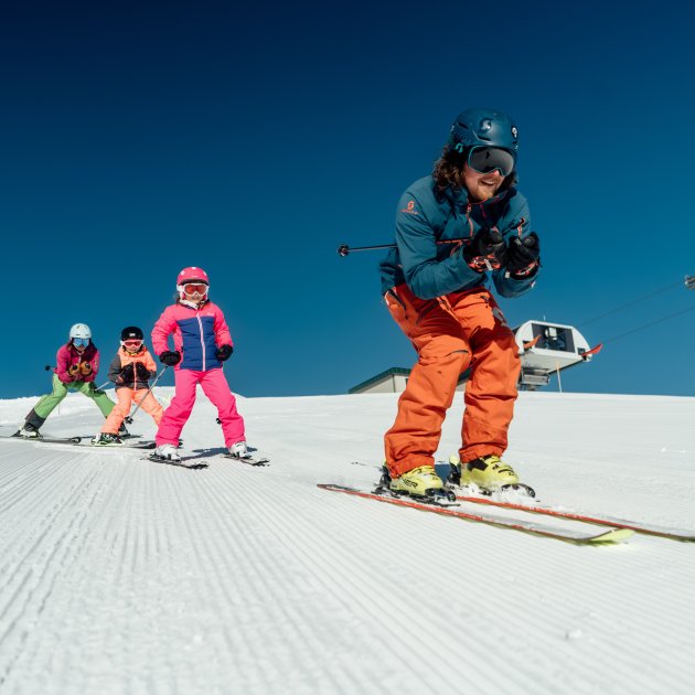 Skilehrer führt Kindergruppe auf der Piste