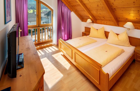Schlafzimmer mit Doppelbett, Holzmöbeln und violetten Vorhängen