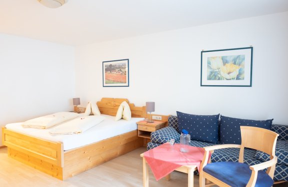 Gemütliches Doppelzimmer mit heller Sitzecke und blauer Couch