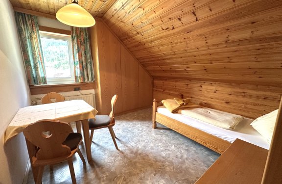 Kleines Zimmer mit Holzdecke, Bett und Esstisch