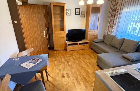 View into the living area with table and two chairs, kitchenette, sofa, and TV