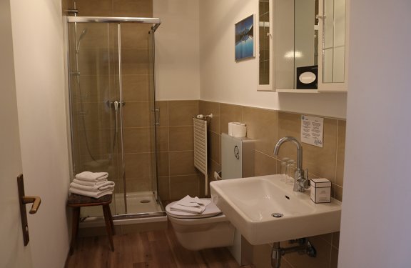 Small bathroom with shower, toilet, sink, and towels stacked on a stool